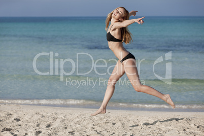 Frau mit Bikini springt fröhlich am Strand Querformat