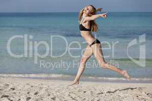 Frau mit Bikini springt fröhlich am Strand Querformat