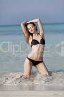 Junge Frau mit schwarzem Bikini am Strand im Wasser Hochformat
