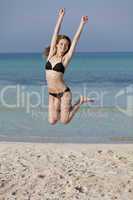 Frau mit Bikini springt fröhlich am Strand Hochformat