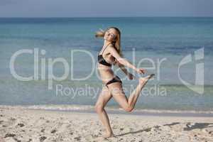 Frau mit Bikini springt fröhlich am Strand Querformat