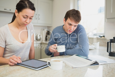 Two people reading from tablet pc and newspaper