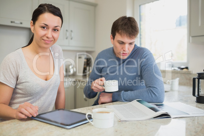 Two people sitting in the kitchen with tablet pc and newspaper