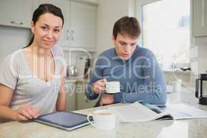 Two people sitting in the kitchen with tablet pc and newspaper