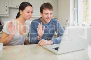 Couple using laptop for video chat and waving