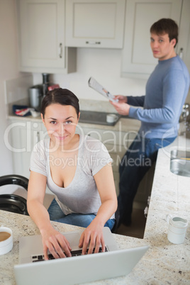 Young woman using laptop with man reading magazine