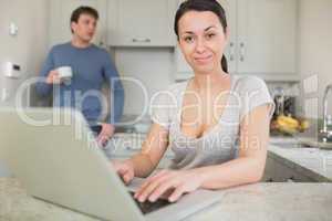 Young woman using laptop with man drinking coffee