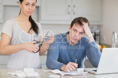 Disappointed couple in the kitchen cutting credit card