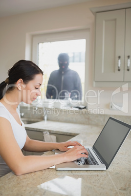 Woman using laptop with robber looking at her through window