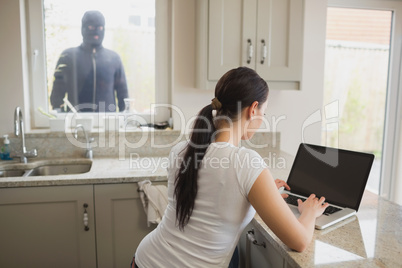 Robber looking at woman using laptop through window
