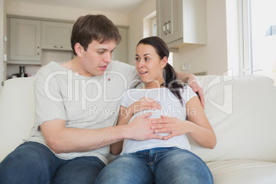 Expectant couple sitting on couch feeling baby kicking