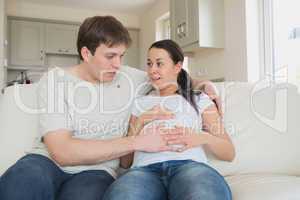 Expectant couple sitting on couch feeling baby kicking