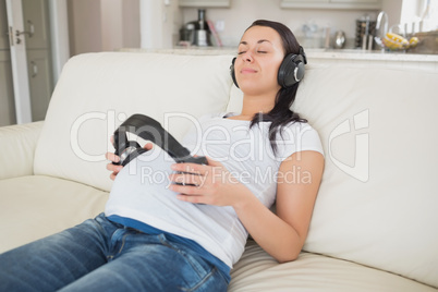 Pregnant woman holding headphones to belly and listening to musi