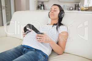 Pregnant woman holding headphones to belly and listening to musi