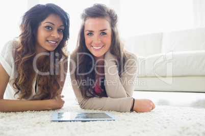 Two friends with a tablet computer while lying on the floor