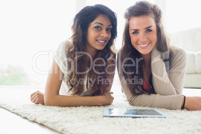 Two smiling friends looking at tablet computer while lying on th