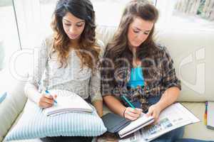 Two women sitting in a couch writing  notepads