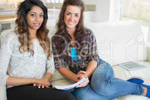 Two women sitting on a couch while writing on a notepad