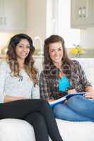Two smiling girls sitting on a couch while writing on a notepad