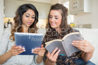 Two girls reading a book and holding a tablet computer