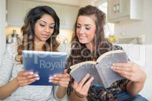 Two girls reading a book and holding a tablet computer