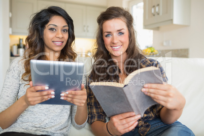 Smiling girls reading a book and holding a tablet computer