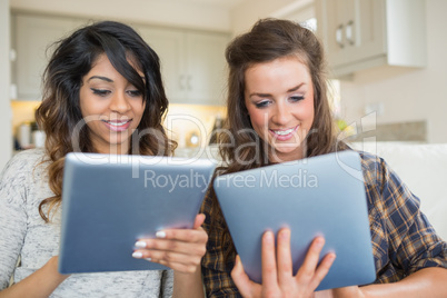 Two smiling women holding and looking at tablet computers