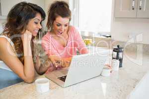 Women looking at laptop and laughing while having coffee