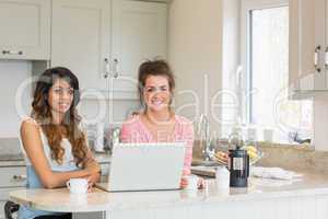 Two smiling friends using laptop and having coffee