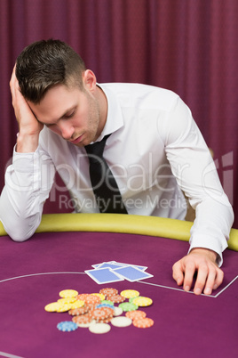 Man leaning on poker table looking disappointed