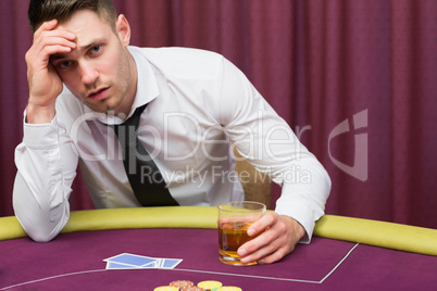 Man leaning on poker table drinking whiskey