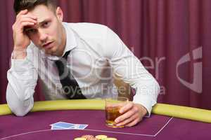 Man leaning on poker table drinking whiskey