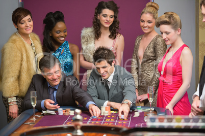 Men playing roulette as women are watching