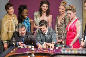 Men playing roulette as women are watching