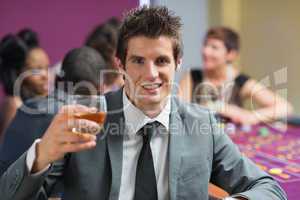 Man raising whiskey glass at roulette table