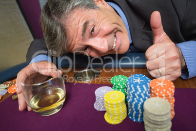 Man leaning on table with whiskey glass giving thumbs up