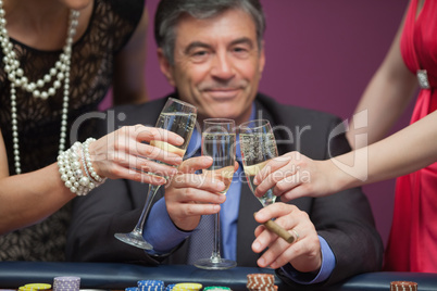 Smiling man sitting while clinking glasses with women