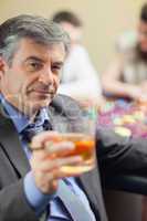 Man lifting glass of whiskey at roulette table