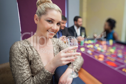 Blonde lifting champagne glass at roulette table