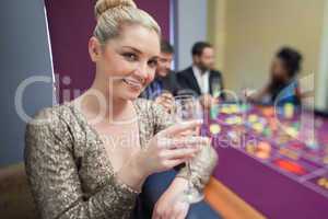 Blonde lifting champagne glass at roulette table