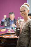 Woman with champagne standing beside roulette wheel