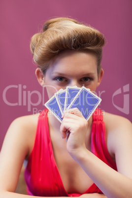 Woman in a casino holding cards before face