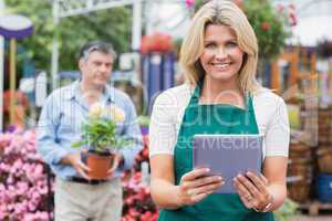 Smiling woman holding a tablet pc with customer holding plant be