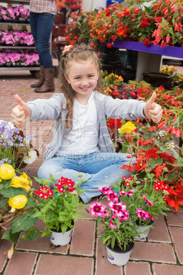 Little girl doing thumbs up sitting in garden centre