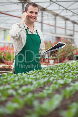 Smiling man on the phone and taking notes in greenhouse