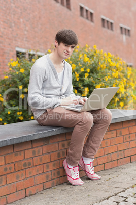 Student sitting on wall with laptop