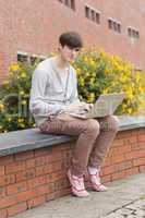 Student sitting on wall with laptop