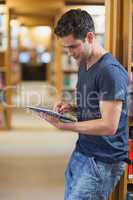 Man leaning against book shelf using tablet pc