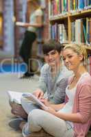 Man and woman sitting in front of a bookshelf while smiling