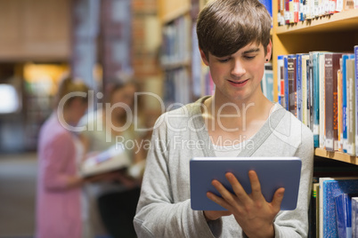 Man leaning at a bookshelf holding a tablet pc